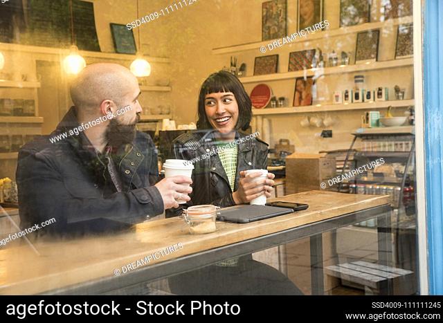 Friends sitting in window of cafe with tablet