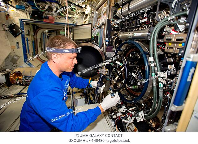 NASA astronaut Reid Wiseman, Expedition 40 flight engineer, performs routine in-flight maintenance on the Multi-user Drop Combustion Apparatus (MDCA) inside the...