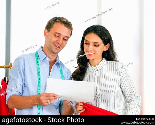 Fashion designer room, man and woman working in home base cloth design business. A male tailor show a shirt design pattern in a paper to young customer while...