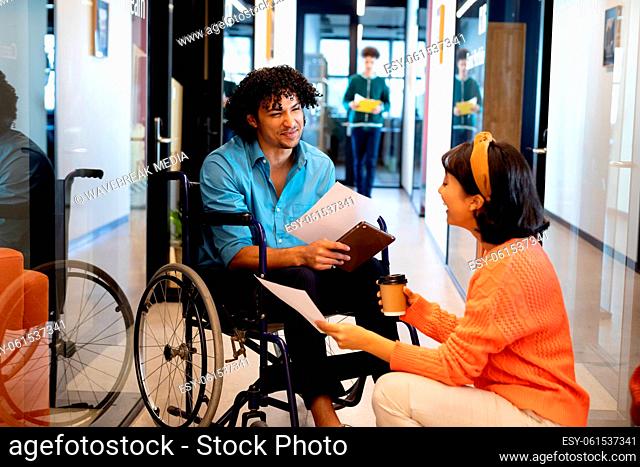 Businesswoman discussing with young businessman sitting in wheelchair at office corridor