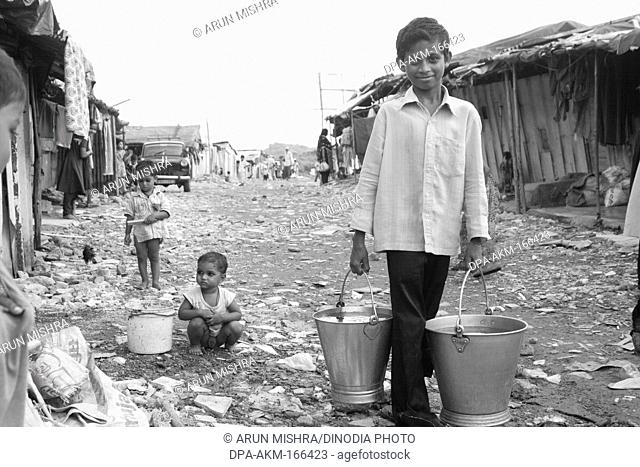 Boy carrying two buckets of water in Malvani slum ; Malad ; Bombay Mumbai ; Maharashtra ; India NO MR
