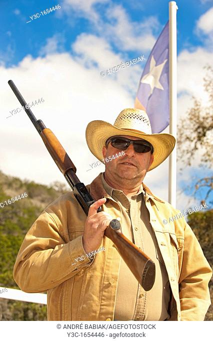 Middle-aged cowboy with firearm in front of Texas flag