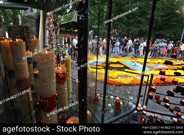 15 August 2023, Bavaria, Ziemetshausen: Pilgrims stand at the pilgrimage site Maria Vesperbild at the Marian grotto, next to a flower carpet lined with candles