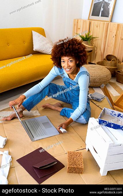Young woman using laptop while sitting on cardboard at home
