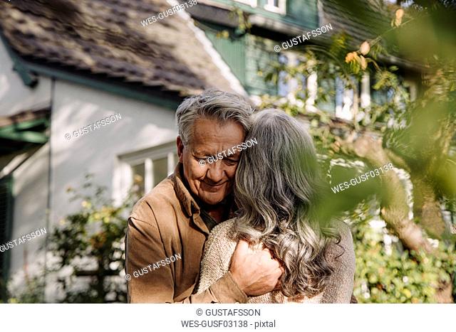 Senior man hugging his wife in garden of their home in autumn