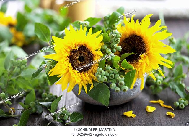 Sunflowers and blueberry sprigs in a ceramic bowl