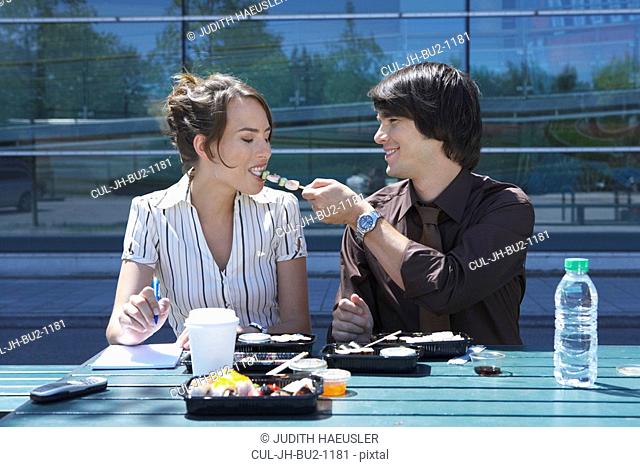 Couple eating sushi together outside while working