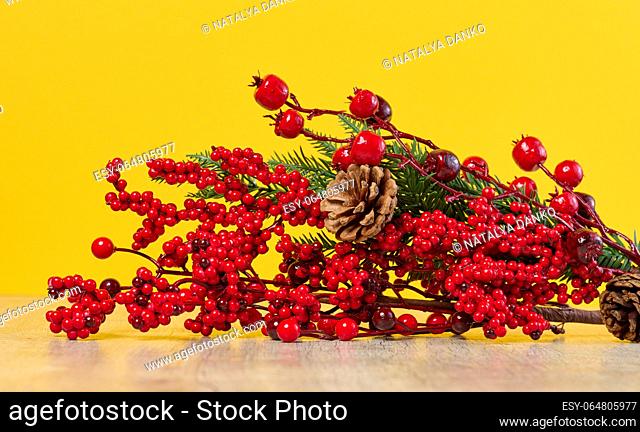 Decorative Christmas branch with red berries and pine cones on a yellow background