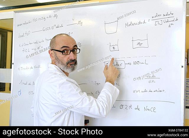 Male teacher in his 50's in a lab coat explaining chemistry on a blackboard. Basque Country, Spain, Europe