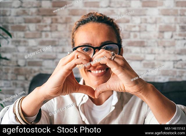 Happy young romantic woman looking at camera through heart shape made of joined fingers. Portrait of caucasian lady showing her love and affection by making...