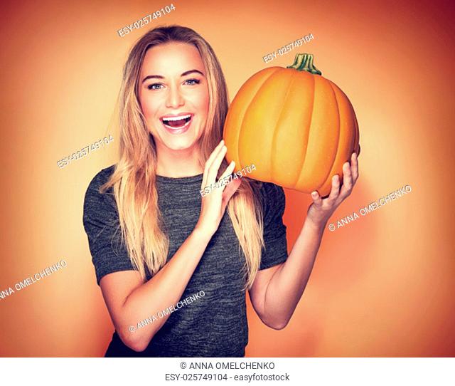 Portrait of beautiful cheerful woman with pumpkin over orange background, celebrating happy Thanksgiving day