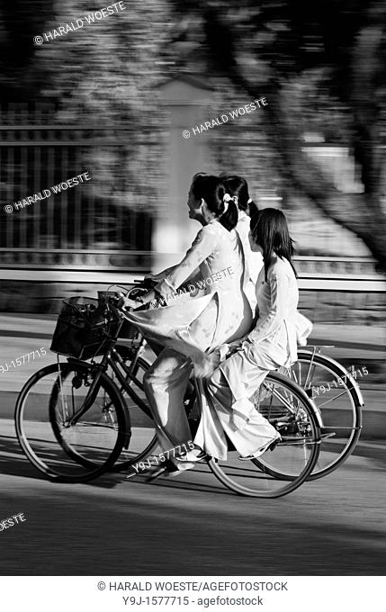 Asia, Vietnam, Hue  Girls in traditional vietnamese white dresses on bicycles returning from school