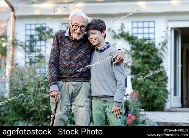 Smiling senior man embracing grandson at backyard