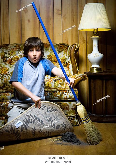 Boy sweeping dirt under rug