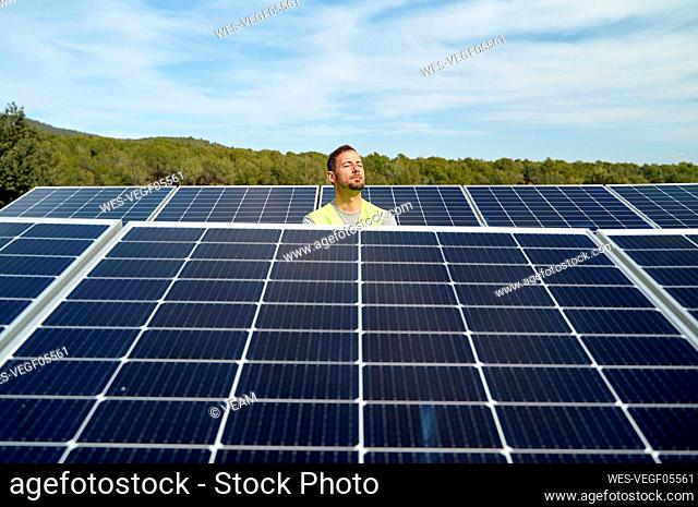 Engineer with eyes closed between solar panels on sunny day