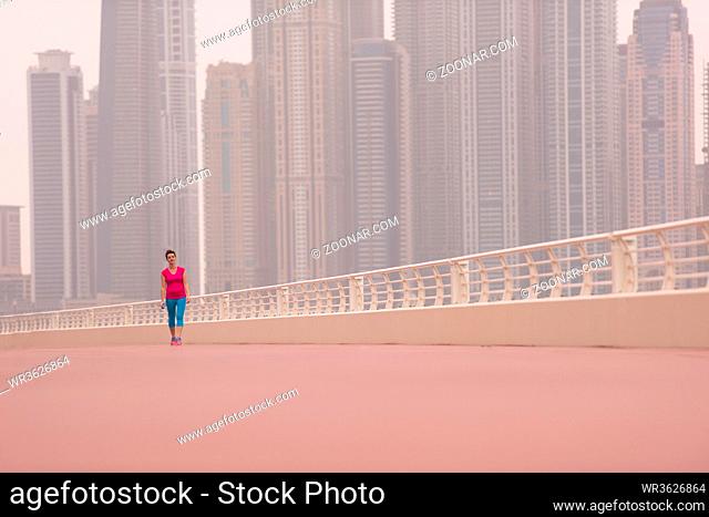 very active young beautiful woman busy running on the promenade along the ocean side with a big modern city in the background to keep up her fitness levels as...