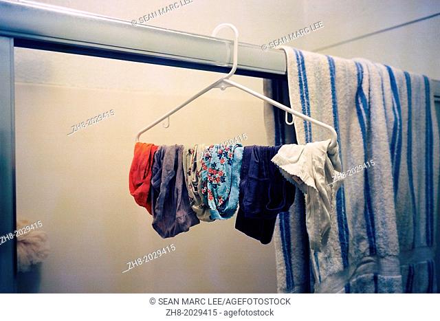 A hanger with dangling women's underwear in a bathroom next to a towel