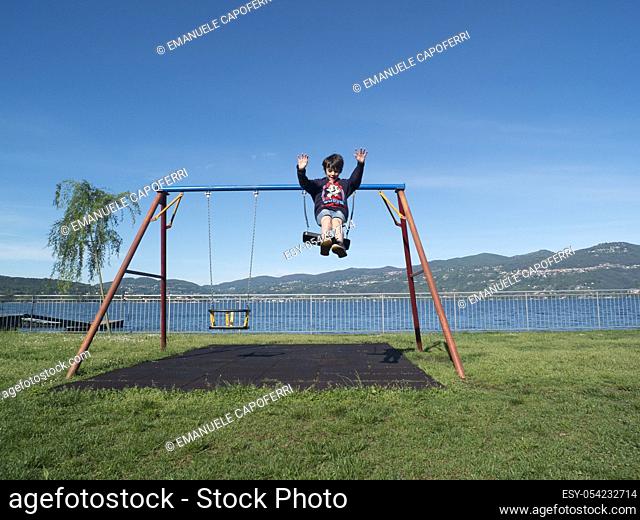 Children play at the playground with swings, Ispra, Varese, Lombardy, Italy