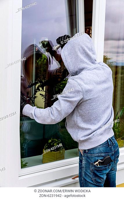 Ein Einbrecher versucht bei einem offenen Fenster mit einer Brechstange einzubrechen