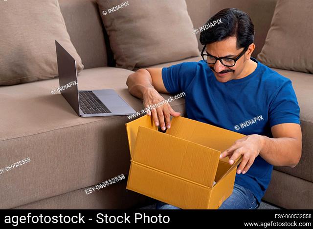 Happy man opening a parcel bought through online at Home