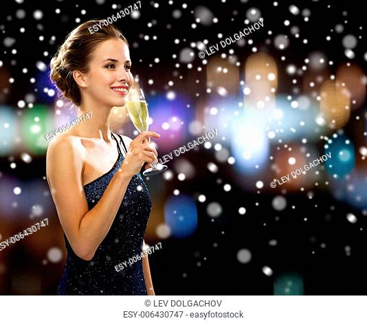 party, drinks, holidays, christmas and people concept - smiling woman in evening dress with glass of sparkling wine over night lights and snow background