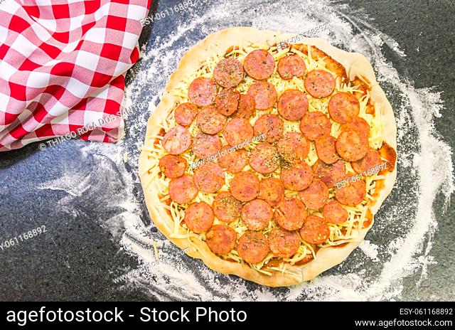 Preparing pepperoni pizza on black granite table