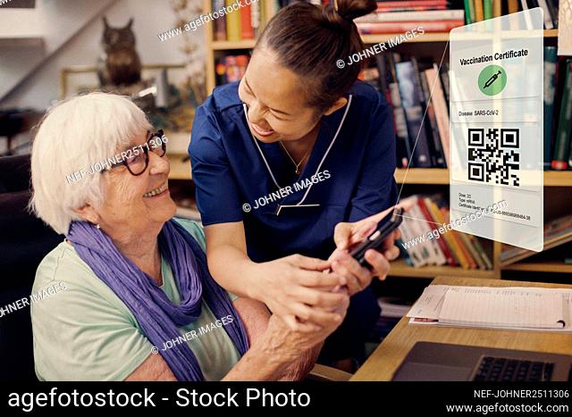 Senior woman and caregiver using cell phone with Covid-19 vaccine certificate