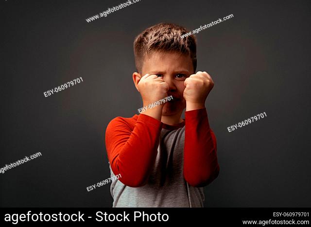 Sad preschool kid expresses anger. Little boy holds his fists in front of him to attack or defend. Conflict concept. Fight concept