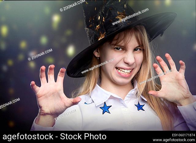 Funny teenage girl wearing Hallow hat makes a frightening gesture on a magical background