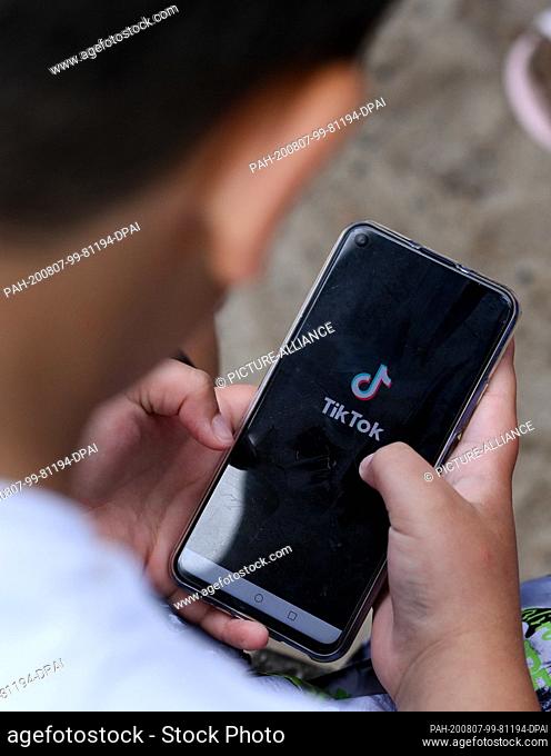 05 August 2020, Berlin: ILLUSTRATION - A boy holds a smartphone in his hands, on which the logo of the short video app TikTok can be seen (posed scene) With...