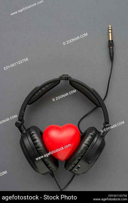 black headphones with red heart, wires and socket on gray background