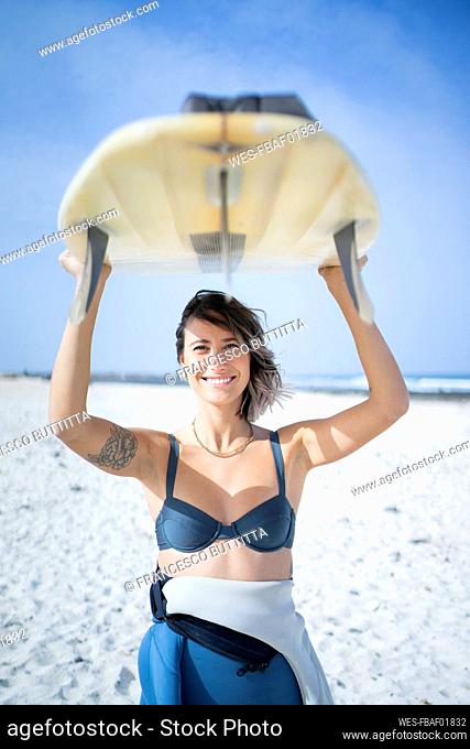 Happy young woman in bikini carrying surfboard at beach on sunny day