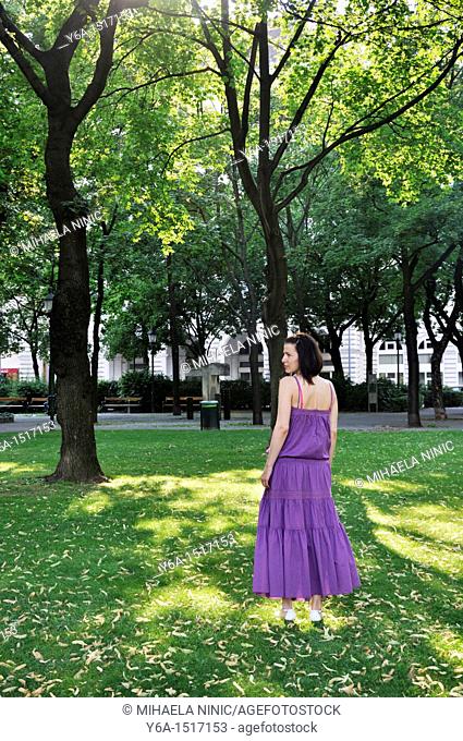 Young woman wearing purple dress standing in a park outdoors