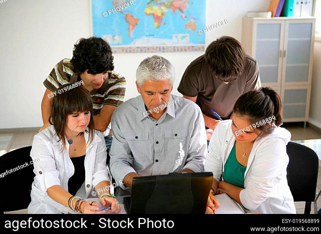 Portrait of young boys and girls in front of a laptop in the classroom next to a
