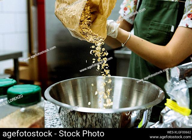 Female baker pouring ingredient in mixing bowl at bakery kitchen