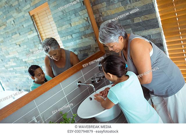 Grandmother and granddaughter washing hands in bathroom sink
