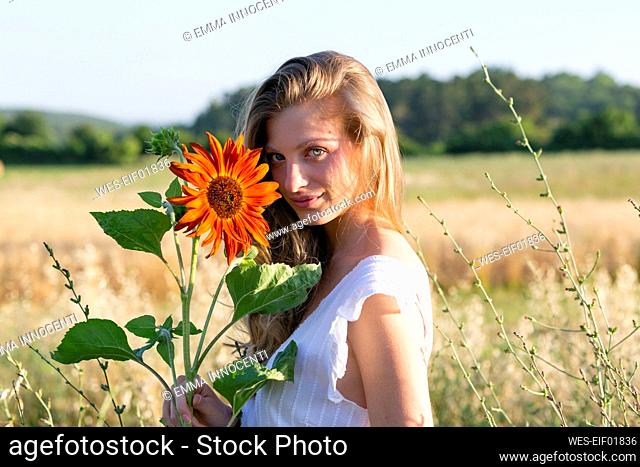 Beautiful young woman with sunflower in field