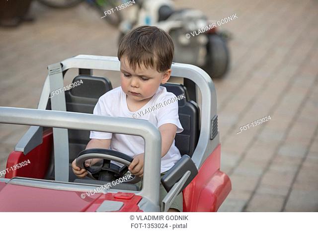 Cute boy sitting in toy car outdoors