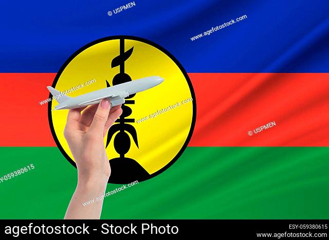 Airplane in hand with national flag of New Caledonia. Travel to New Caledonia