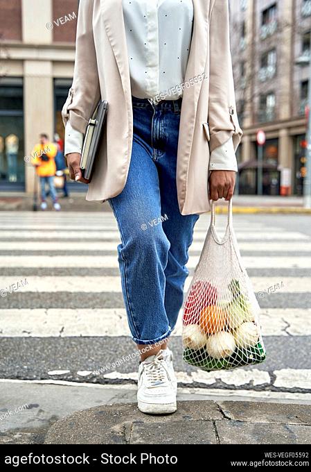 Businesswoman walking at street holding fruits in mesh bag