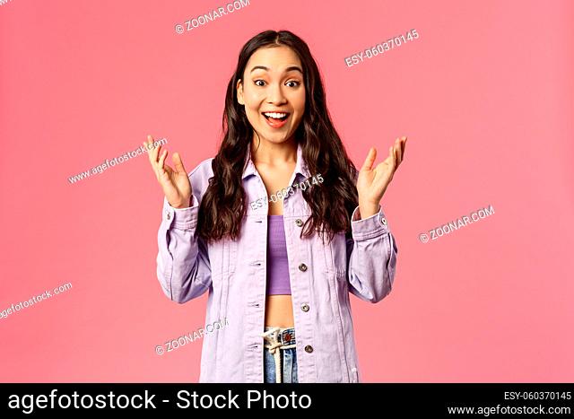 Portrait of surprised, enthusiastic korean girl in denim jacket, look wondered and happy, hear great news, applause, raise hands to clap and praise great work