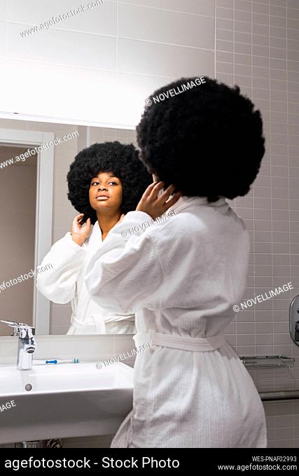 Young woman with hand in hair looking in mirror in home