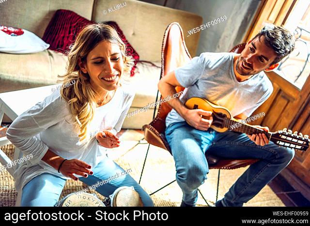 Happy young couple playing duet with drums and guitar in living room at home