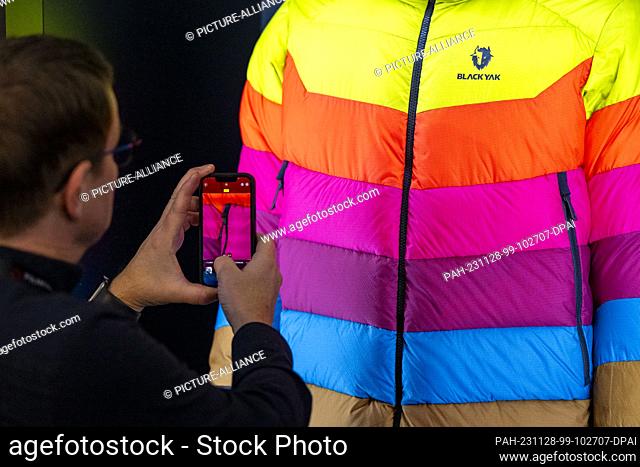 28 November 2023, Bavaria, Munich: A trade fair visitor takes a photo of a Black Yak winter jacket during the ISPO sporting goods trade fair at Messe München