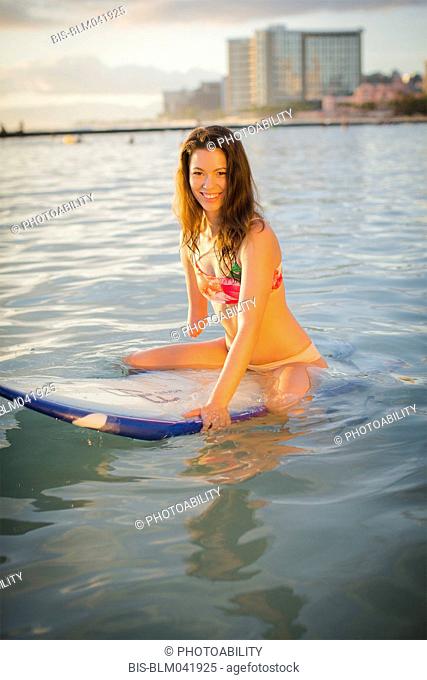 Mixed race amputee sitting on surfboard in ocean