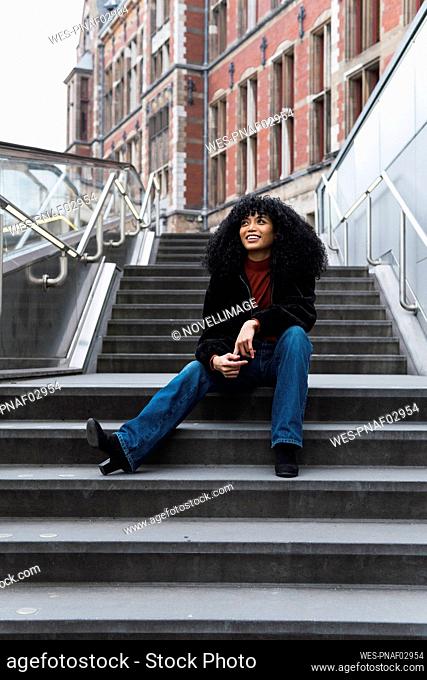 Cheerful young woman sitting on staircase in city