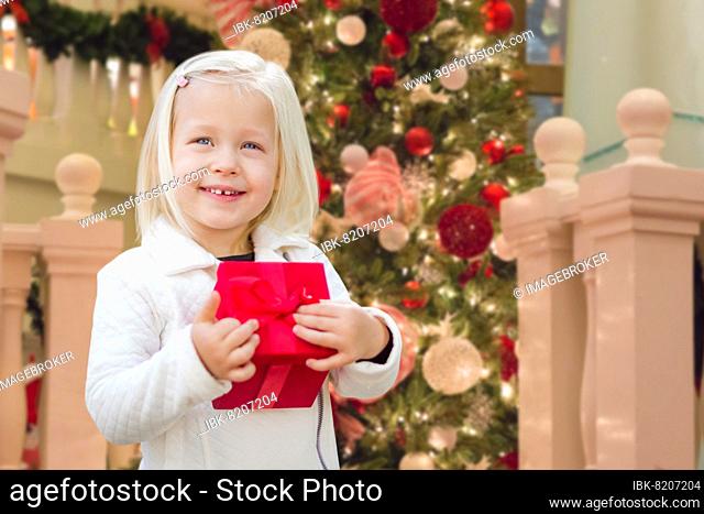 Happy young girl holding gift box in front of decorated christmas tree