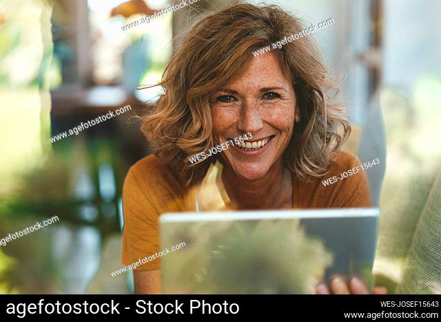 Happy mature woman with tablet PC seen through glass window