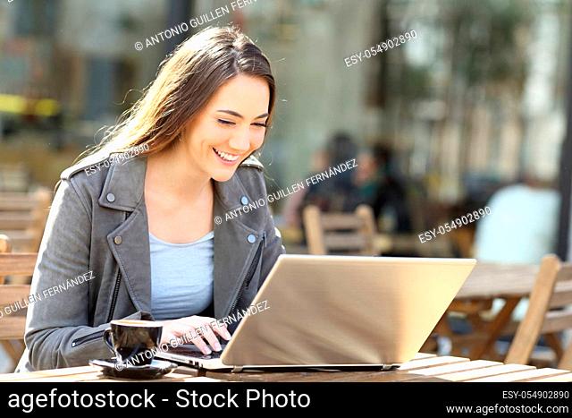 Happy woman typing on her laptop sitting on a coffee shop terrace