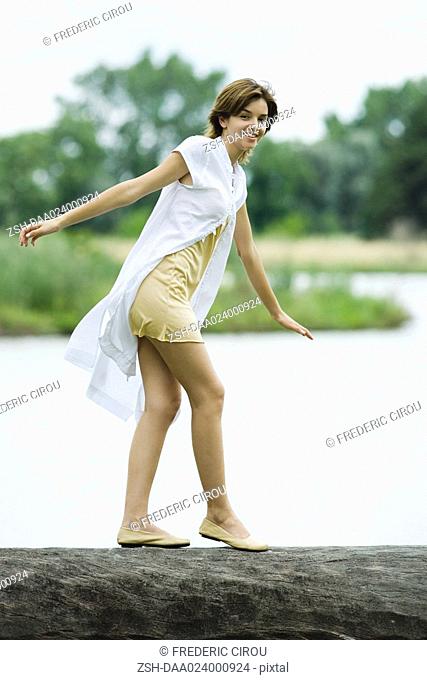 Young woman walking across log with arms out, smiling at camera